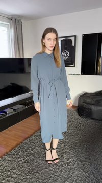 Μακρύ, πουκαμισοειδές φόρεμα σε ανοιχτό μπλε ύφασμα, με δεμένη μέση, μακριά μανίκια και ευθεία γραμμή. Συνδυασμένο με μαύρα σανδάλια με τακούνι.