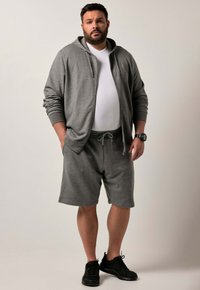 Felpa grigia con cappuccio e lacci, abbinata a pantaloni corto grigi. Scarpe da ginnastica nere. Design semplice e casual con una vestibilità comoda.