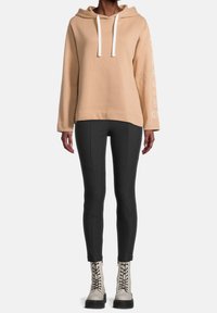 Beige hoodie med vita dragsnören, parat med mörkgrå tajta leggings. Skorna har snörning och en kraftig sula.