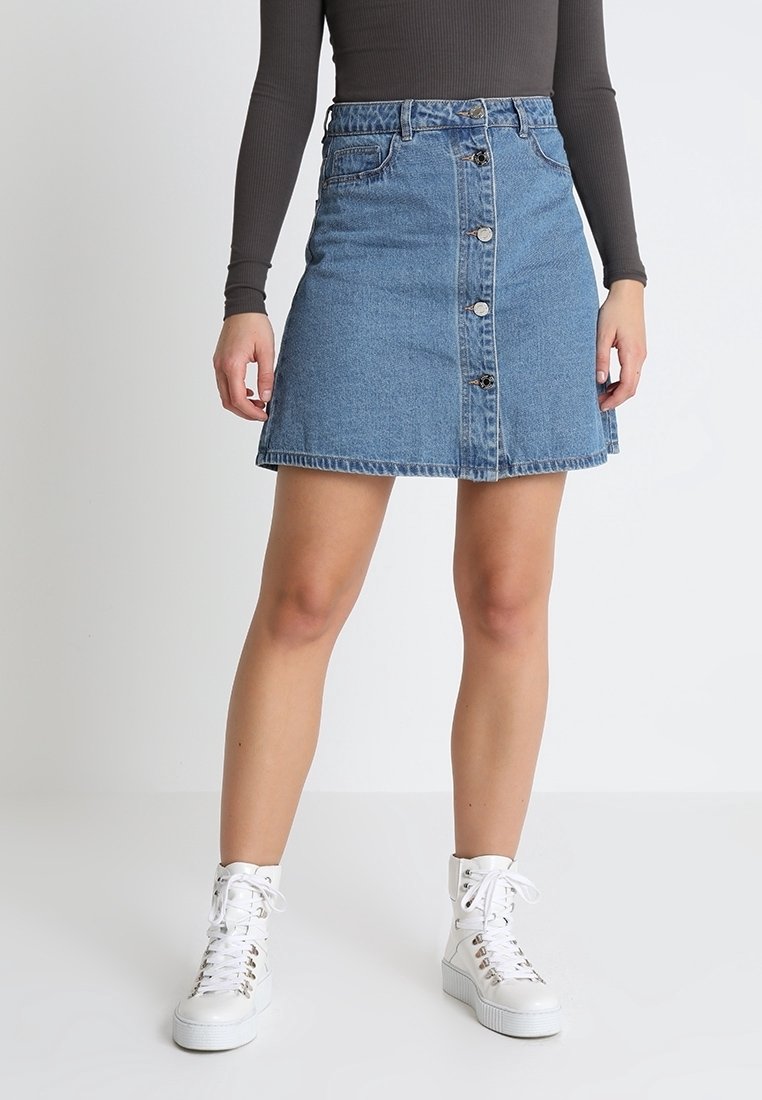 Jeans A-Linien-Rock, hellblau, mit Knopfverschluss, fünf Taschen und Kontrastnähten. Kombiniert mit weißen High-Top-Sneakern.