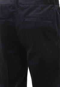 Donkerblauwe ribfluwelen broek met verticale geribbelde textuur, twee achterzakken en een getailleerde pasvorm, met een gladde tailleband voor comfort.