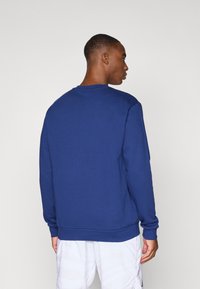 Μπλε σκούρο φούτερ με μακριά μανίκια και στρογγυλή λαιμόκοψη, κατασκευασμένο από υφή ύφασμα. Διαθέτει ριμπ τελείωμα στη μέση και λεπτομέρειες σε μανσέτες.