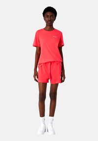 Lys koralfarvet T-shirt og shorts sæt lavet af bomuld, med en afslappet pasform, elastisk talje og broderet logo detaljer. Hvide sneakers fuldender looket.