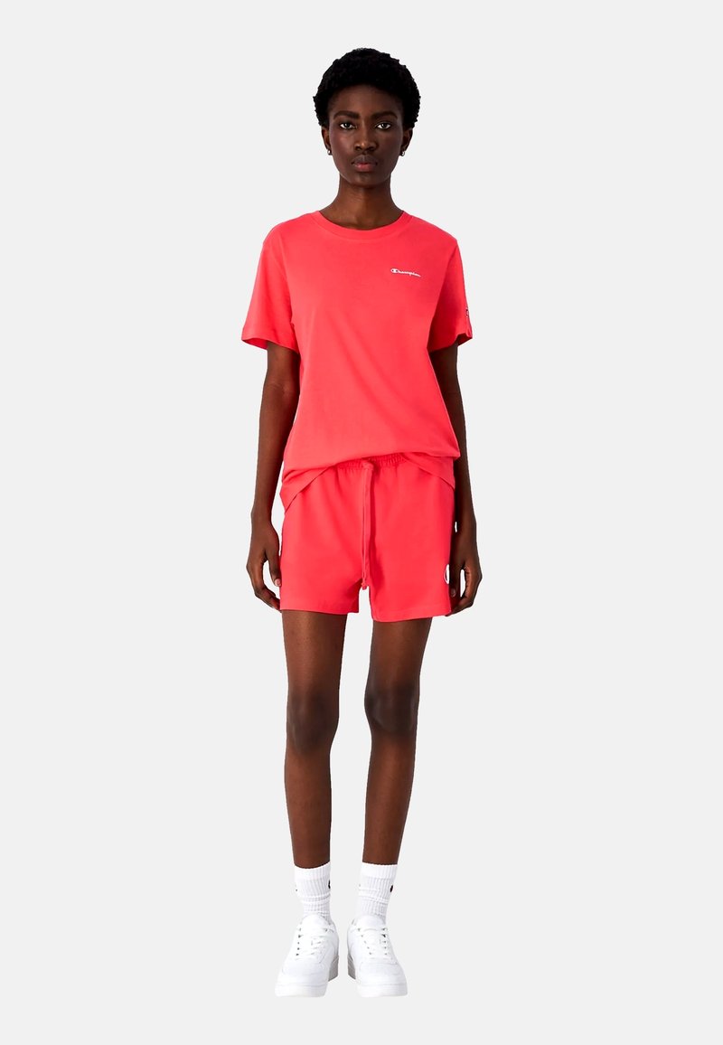 Lys koralfarvet T-shirt og shorts sæt lavet af bomuld, med en afslappet pasform, elastisk talje og broderet logo detaljer. Hvide sneakers fuldender looket.