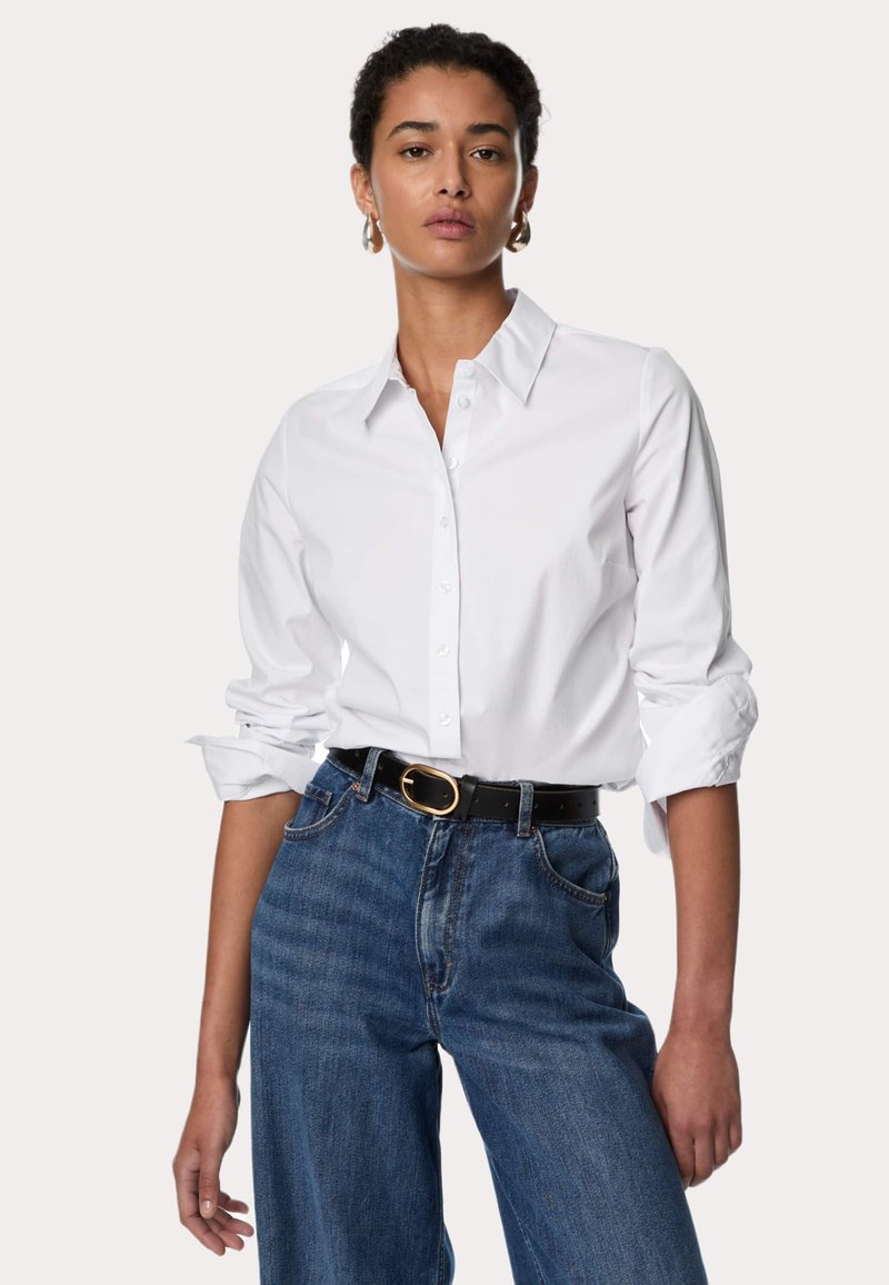 Witte blouse met lange mouwen en een klassieke kraag, gecombineerd met hoge blauwe denim spijkerbroek en een zwarte riem met een gouden gesp.