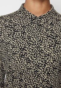 Camicia button-up nera e crema con colletto, caratterizzata da un motivo astratto testurizzato e bottoni arrotondati. Vista ravvicinata dei dettagli del tessuto.