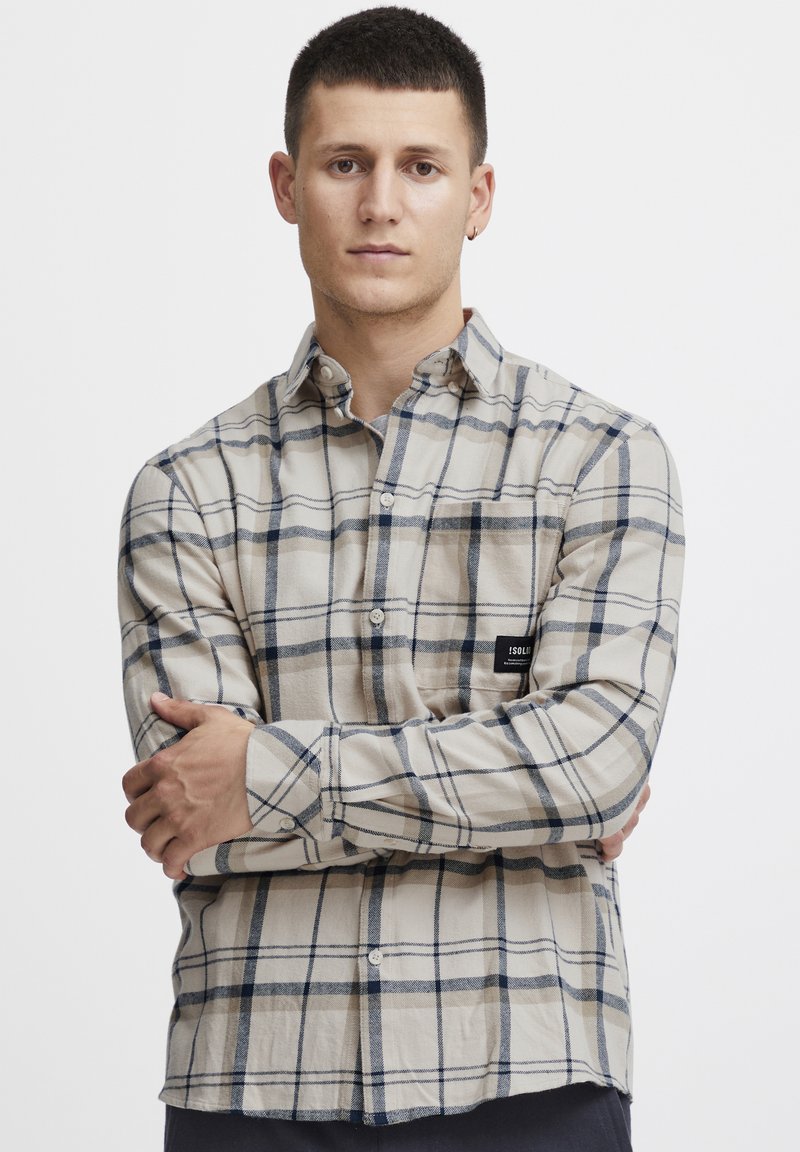 Camicia a scacchi beige con linee blu navy e grigie, realizzata in tessuto leggero, dotata di taschino sul petto con etichetta del marchio.