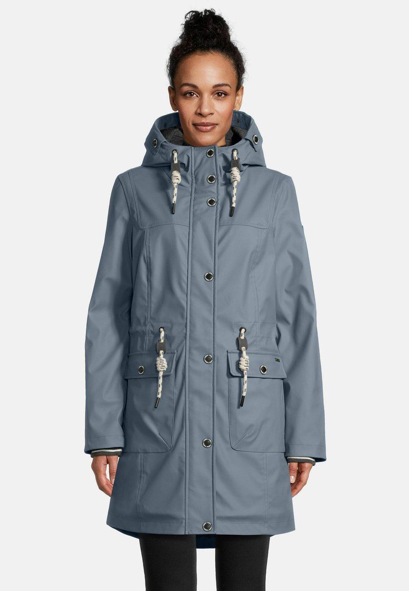 Woman wearing a blue hooded raincoat with white rope toggles and snap buttons, standing against a plain light background.