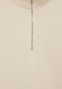 Lysebeige trøje med lynlås og høj krave, der har en metallisk lynlås og glat stofstruktur. Minimalistisk design og rene linjer.