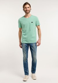 Gestreept mintgroen t-shirt met een ronde hals en klein zwart logo, gecombineerd met lichtblauwe jeans en crèmekleurige sneakers.