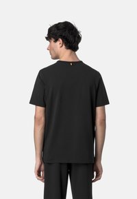 T-shirt nera a maniche corte realizzata in tessuto morbido, con collo a giro e una piccola etichetta gialla sul retro. Design semplice e minimalista.