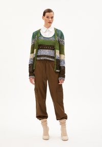 Mehrfarbiger gestrickter Pullover mit grünen, blauen und braunen Streifen, kombiniert mit braunen Cargo-Hosen und cremefarbenen strukturierten Knöchelsocken.