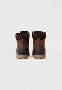 Botas de cuero marrón con un collar de ante, suela de goma y logotipo de la marca en relieve en la parte posterior. Presenta una punta redonda y un diseño robusto.