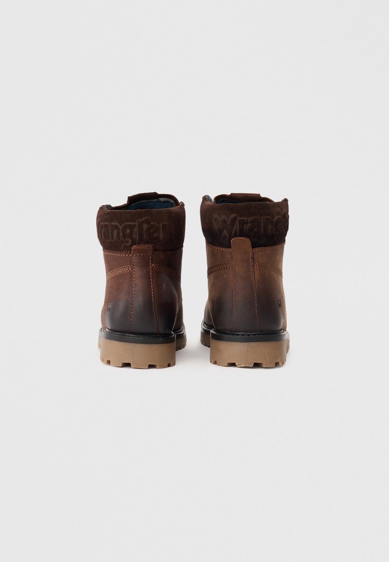 Braune Lederstiefel mit einem Wildlederkragen, Gummisohle und geprägtem Markenlogo auf der Rückseite. Sie verfügen über eine runde Zehenform und ein robustes Design.