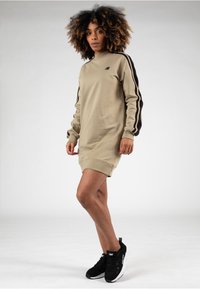 Vestido de sudadera color caqui con cuello alto, mangas largas con franjas negras y puños acanalados. Combinado con zapatillas negras.