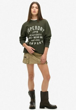 Sudadera verde oliva con texto blanco, falda cargo beige con bolsillos y botas negras hasta el tobillo. Diseño simple y casual, tela suave.