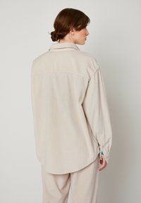 Ljusbeige kordflorenskjorta, knapplås-colle, långärmad med manschettdetalj och rundad nederkant. Texturerad tyg med vertikala ränder.