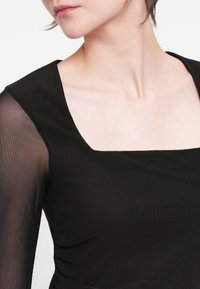 Rochie neagră cu decolteu pătrat și mâneci lungi din material transparent. Prezintă un țesut texturat cu pliuri subtile pe lateral pentru conturare.