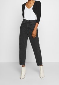 Mustat korkeavyötäröiset farkut rentolla istuvuudella, yhdistettynä valkoiseen V-kaulaiseen toppiin ja kermanvärisiin nilkkureihin. Tasainen, sileä pinta, minimaalinen koristelu.