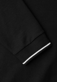 Czarny rękaw bluzy z prążkowanym mankietem ozdobionym białym paskiem. Tkanina wydaje się miękka i fakturowana, co wskazuje na codzienny, swobodny styl.