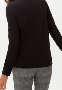 Černý dlouhý rukáv s rovný střih, s jednoduchým švem na zádech. Nosený s šedými kostkovanými kalhotami. Měkká tkanina, minimalistický design.