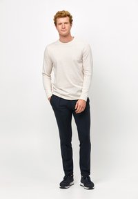 Hellbeige Langarmshirt mit Rundhalsausschnitt, kombiniert mit schmal geschnittenen, dunkelblauen Hosen und schwarzen Sportschuhen. Einfaches, lässiges Design.