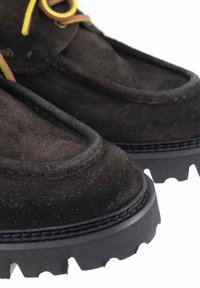 Scarpe in suede marrone con punta arrotondata, lacci gialli e verdi a contrasto, e una suola in gomma nera spessa con un motivo di battistrada.