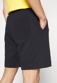 Shorts en coton noir avec une ceinture élastique, des poches latérales et une poche plaquée arrière. Texture lisse et finition ourlet propre.