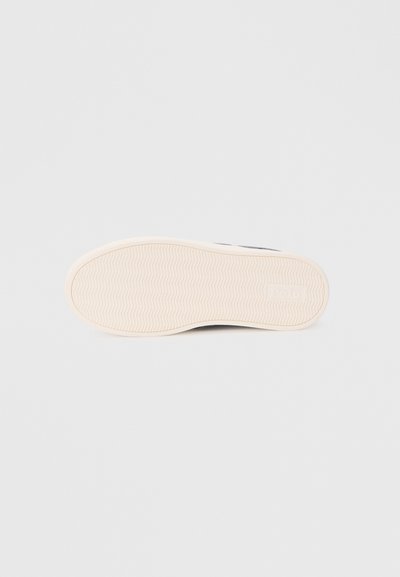 Sola do sapato com uma superfície texturizada em bege, apresentando um padrão ondulado e um logótipo da marca "Polo" em relevo na lateral.