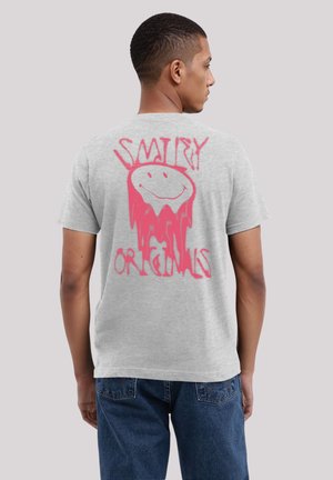 Graues T-Shirt mit einem großen pinken Aufdruck auf der Rückseite, der ein lächelndes Gesicht zeigt, und dem Text „SMIRY ORIGINALS“ im tropfenden Stil.