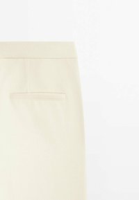 Pantalon beige ajusté en tissu texturé, doté d'une taille standard et d'une seule poche arrière avec une ouverture horizontale.