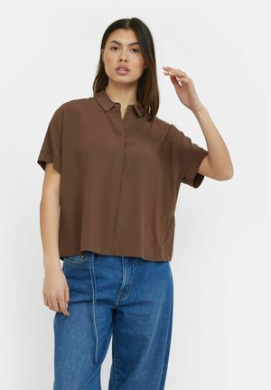 Brown short-sleeve shirt with a collar, lightweight fabric, relaxed fit, and a straight hem. Paired with blue high-waisted jeans.