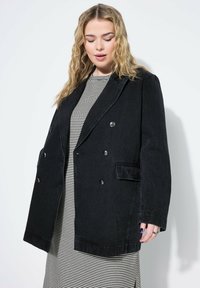 Mustapari denim kaksoisnapillinen takki, jossa on suuret napit ja sivutaskut. Päällä mustavalkoinen raidallinen paita, jossa on rento istuvuus.