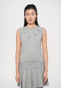 Maglione senza maniche grigio con applicazioni floreali testurizzate sul davanti, scollo e orlo a coste, abbinato a una gonna grigia plissettata.