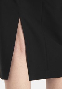 Jupe noire avec une fente latérale, texture lisse, design ajusté et lignes épurées. Le tissu semble léger et durable.