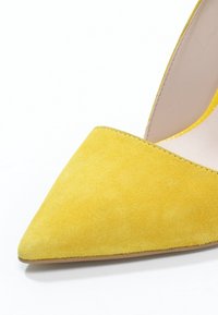 Chaussure à talon haut en daim jaune avec un bout pointu et une doublure intérieure lisse. La semelle extérieure est marron clair avec peu de détails texturés.