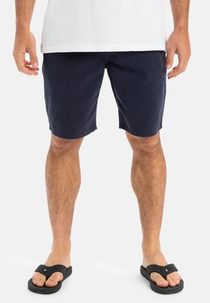 Mørkeblå shorts i et let materiale, med lige snit og sidelommer. Båret med sorte flip-flops for et afslappet look.