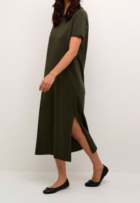 Oliivinvihreä, lyhythihainen maksimekko, jossa on sivuaukot, valmistettu pehmeästä kankaasta, yhdistettynä mustiin ballerinatossuihin. Yksinkertainen, rento muotoilu.