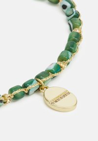 Groene kralenarmband met een gouden charme met een gestructureerd oppervlak en kristalaccenten, vakkundig gevlochten met gouden draad.