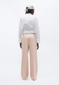 Fehér galléros ing, hátrakötött dizájnnal, magas derekú, bőszárú rózsaszín nadrággal párosítva. A szett mintás sállal kiegészítve.