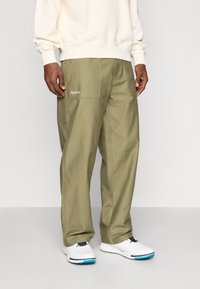 Pantaloni cargo de culoare verde măslin, cu multiple buzunare și un logo brodat alb. Asortați cu pantofi albi cu un accent albastru.