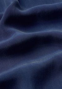 Tela azul oscuro con una textura suave, que presenta sutiles degradados y pliegues suaves que crean una apariencia ondulada.