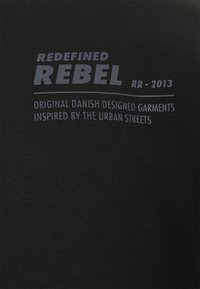 Tissu noir avec le texte : 'REDEFINED REBEL RR 2013' et 'Vêtements originaux conçus au Danemark et inspirés par les rues urbaines.'