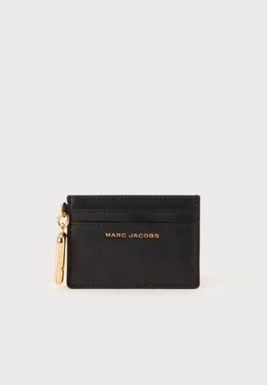Porte-cartes en cuir noir avec tirette de fermeture éclair dorée et logo MARC JACOBS embossé en doré au centre devant.