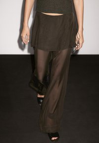 Ensemble en deux pièces composé d'un haut tricoté court vert foncé et d'un pantalon transparent en couches vert foncé, associé à des sandales à talons hauts noires.