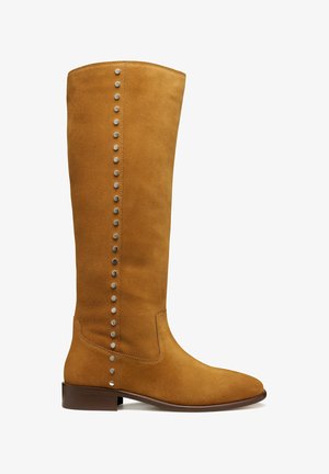 Bota alta de ante marrón claro con tacón bajo de madera y fila vertical de tachuelas plateadas en el lado exterior.