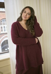 Maglione borgogna lavorato a maglia con scollatura a V, maniche lunghe e vestibilità ampia, caratterizzato da un tessuto strutturato e fessure laterali.