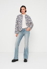 Veste à imprimé floral blanc et marine, avec un col rond. Associée à un jean évasé bleu clair et des chaussures à plateforme noires.