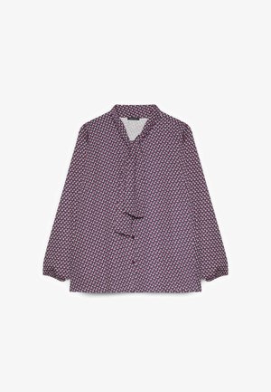 Blusa a maniche lunghe con motivo geometrico in viola, bianco e rosa e un fiocco annodato al collo, mostrata su uno sfondo bianco.
