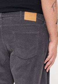 Grijze corduroy broek met een gestructureerd, verticaal ribpatroon. Heeft een bruine label op de tailleband en een achterzak met patch.